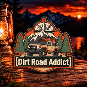 May include: A rectangular patch with rounded edges featuring a tan off-road vehicle, green pine trees, and a compass rose set against a mountain backdrop. The text "Dirt Road Addict" is printed in white capital letters within a dark green border.