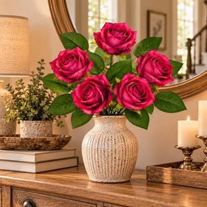 May include: A bouquet of five deep pink roses with green leaves arranged in a cream-coloured, vertically ribbed ceramic vase with a speckled finish. The roses are fully bloomed with layered petals, and the vase has a rounded body and a narrow neck.