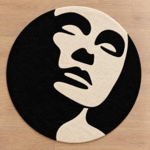 May include: A circular area rug featuring a high-contrast black and cream design. The pattern depicts a stylized, abstract human face in profile, with the cream-colored facial features set against a solid black background, creating a bold graphic.