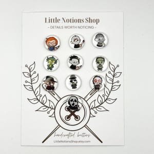 May include: A set of ten circular buttons featuring cartoon horror character illustrations, displayed on a white card labeled Little Notions Shop - DETAILS WORTH NOTICING - with a graphic of crossed needles and a large button at the bottom.