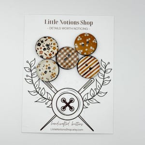 May include: Five round buttons attached to a display card labeled Little Notions Shop. The buttons feature various patterns including floral prints in cream and mustard, a brown and white gingham check, and brown and white diagonal stripes.