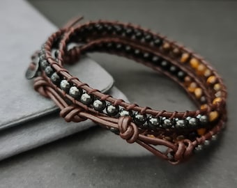 May include: A brown leather wrap bracelet with black and brown beads. The bracelet is wrapped around a gray surface.