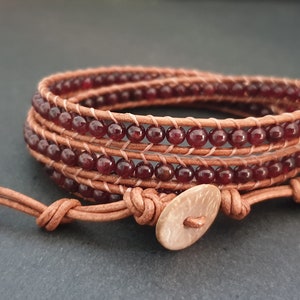 May include: A brown leather wrap bracelet with a brown button closure and red gemstone beads.