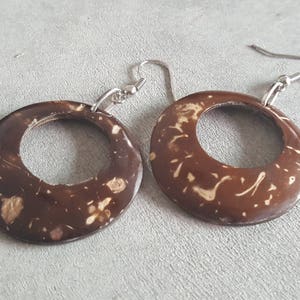 May include: A pair of brown coconut shell earrings with silver hooks. The earrings are round and have a natural, marbled pattern.