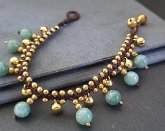 May include: A brown cord bracelet with gold beads and green jade stones. The bracelet has a tassel on one end.
