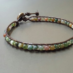 Könnte beinhalten: Ein braunes Lederarmband mit einer Reihe von mehrfarbigen Achatperlen.