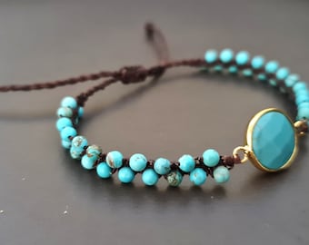 Puede incluir: Un brazalete de cuentas turquesa con un dije de piedra turquesa más grande. El brazalete está hecho con cordón marrón y tiene un cierre de nudo deslizante.