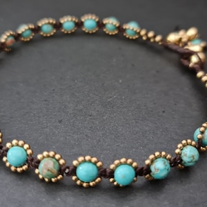 Könnte beinhalten: Ein türkisfarbenes und goldenes Armband mit brauner Kordel.