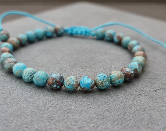 Puede incluir: Un brazalete de cuentas turquesa y marrón con cierre de cordón azul.
