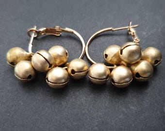 May include: A pair of gold hoop earrings with multiple small gold bells attached. The bells are clustered together and hang from the hoops.