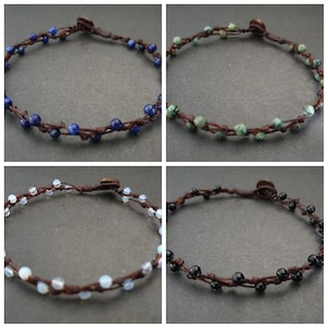 May include: Four handmade bracelets with different colored beads. Each bracelet is made with brown cord and features a wooden button closure. The beads are blue, green, white, and black.