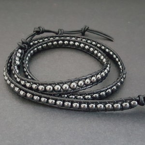 Könnte beinhalten: Ein schwarzes Lederarmband mit silbernen Perlen. Das Armband hat einen Magnetverschluss.