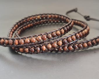 May include: A brown leather wrap bracelet with brown wooden beads. The bracelet has a button closure.