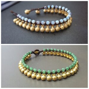 May include: Two anklets with gold beads and a brown cord. The top anklet has light blue beads and the bottom anklet has green beads.
