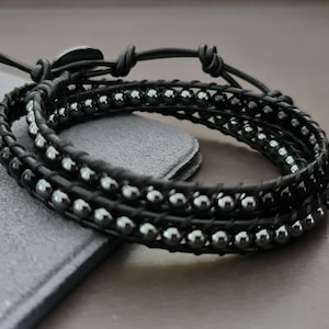 May include: A black leather wrap bracelet with black hematite beads. The bracelet is made of three strands of leather and has a simple knot closure.