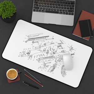 May include: A rectangular desk mat featuring a white surface with a detailed black technical line drawing of a firearm assembly diagram. The print includes numerous individual components labeled with small numbers, showcasing the internal parts.