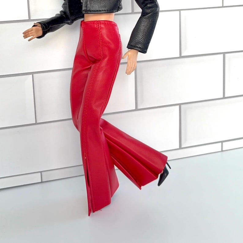 May include: A doll in a black leather jacket and red faux leather trousers. The trousers have a flared leg design with a slit at the ankle. The doll is also wearing black high heels.