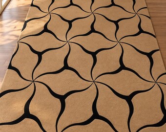 Op de afbeelding: Een rechthoekig vloerkleed met een beige basiskleur en een herhalend zwart geometrisch patroon van gebogen, in elkaar grijpende vormen die een doorlopend, vloeiend ontwerp creëren over het gehele oppervlak van de vloerbedekking.