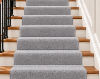 Op de afbeelding: Een set lichtgrijze trapmatten geïnstalleerd op een houten trap. Elke rechthoekige mat bedekt het midden van de trede en is voorzien van een zachte, getextureerde pool en afgewerkte randen die contrasteren met de natuurlijke bruine houtafwerking.