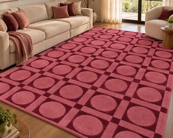 Op de afbeelding: Een groot rechthoekig vloerkleed met een herhalend geometrisch patroon van donkerrode vierkanten en cirkels op een lichtere roze achtergrond. Het ontwerp bestaat uit een raster van vierkanten met gecentreerde cirkels voor een textuur.