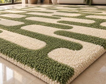 Puede incluir: Una alfombra rectangular con textura de pelo alto y mechones, que presenta un patrón geométrico repetitivo de formas redondeadas tipo píldora. El diseño alterna entre secciones de color verde oliva intenso y color crema.