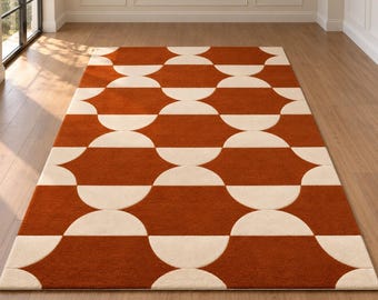 Op de afbeelding: Een rechthoekig vloerkleed met een herhalend geometrisch patroon van in elkaar grijpende halve cirkels in gebrand oranje en crème. Het ontwerp bestaat uit rijen afgeronde vormen die een doorlopend, symmetrisch motief over het oppervlak vormen.