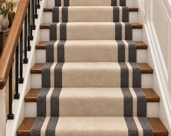 Op de afbeelding: Een trap met een centrale tapijtloper met een lichtbeige midden en twee donker antracietgrijze strepen die verticaal langs de zijkanten lopen. De trap heeft houten treden en witte stootborden, aangevuld met een houten leuning en zwarte balusters.