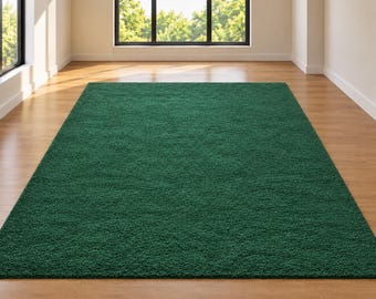 Op de afbeelding: Een rechthoekig vloerkleed in een diepe bosgroene kleur met een dikke, pluche, hoogpolige textuur. Het kleed ligt plat op een lichtgekleurde houten vloer en beslaat een aanzienlijk deel van de centrale vloeroppervlakte in de kamer.