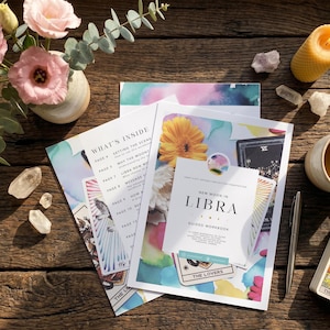 Op de afbeelding: Een New Moon in Libra werkboek met een kleurrijk bloemen- en tarotkaartontwerp op de kaft. Het werkboek bevat een inhoudsopgave met de titel What's Inside, een zilveren pen, een set tarotkaarten, een gele kaars en heldere kristallen.