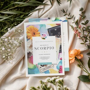 Puede incluir: Un libro de ejercicios guiado New Moon in Scorpio con una cubierta blanca e ilustraciones coloridas de flores y cartas del tarot. El texto dice New Moon in Scorpio Guided Workbook, junto a detalles como The Lovers.