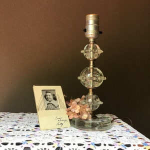 May include: A vintage clear glass lamp with three spherical sections and a brass base. A small framed photograph and pink flowers sit beside the lamp. The photograph has the inscription "Love always, Betty."