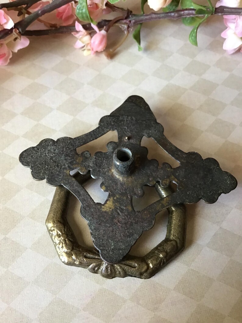 Peut inclure: Tirette de tiroir en laiton antique avec un design orn&eacute;. La tirette pr&eacute;sente une finition sombre et patin&eacute;e sur la plaque arri&egrave;re et une poign&eacute;e en anneau hexagonale. Le design comprend des d&eacute;tails floraux et des volutes, ajoutant une esth&eacute;tique vintage.