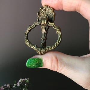 May include: Ornate antique brass drawer pull with a decorative floral design. The pull features a central stem and a curved, open handle. The brass has a slightly aged, tarnished appearance, adding to its vintage charm.