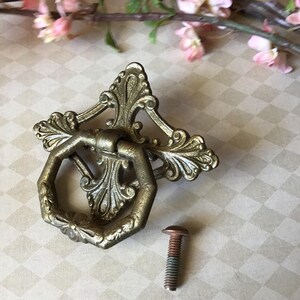 Peut inclure: Tirette de tiroir en laiton orn&eacute; avec une plaque arri&egrave;re d&eacute;corative et une poign&eacute;e hexagonale. Une vis assortie est incluse. La quincaillerie a une finition antique et est probablement destin&eacute;e &agrave; une armoire ou une commode. Le fond a un motif de losanges.