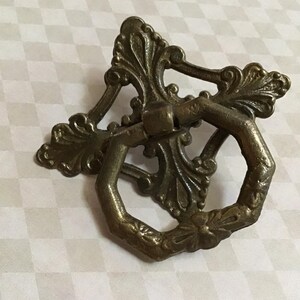 Peut inclure: Poign&eacute;e de tiroir antique en laiton orn&eacute; d'un motif floral et de feuilles d&eacute;coratif. La poign&eacute;e comporte une poign&eacute;e en anneau et une plaque arri&egrave;re &eacute;labor&eacute;e, id&eacute;ale pour la restauration de meubles anciens.