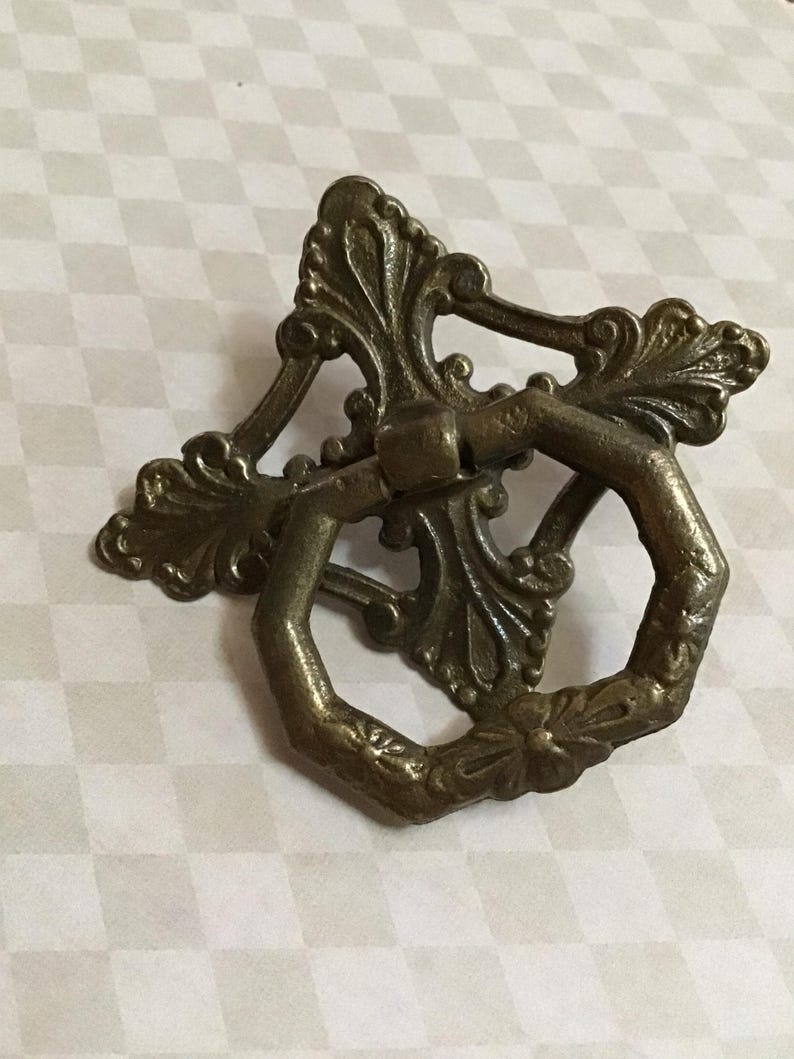 Peut inclure: Poign&eacute;e de tiroir antique en laiton orn&eacute; d'un motif floral et de feuilles d&eacute;coratif. La poign&eacute;e comporte une poign&eacute;e en anneau et une plaque arri&egrave;re &eacute;labor&eacute;e, id&eacute;ale pour la restauration de meubles anciens.