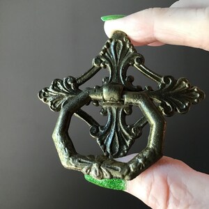 Peut inclure: Tirette de tiroir en laiton antique orn&eacute;e d'un motif floral d&eacute;coratif. La tirette pr&eacute;sente une poign&eacute;e hexagonale et une plaque arri&egrave;re d&eacute;taill&eacute;e avec des motifs de feuilles sym&eacute;triques. Une pi&egrave;ce de quincaillerie de style vintage.