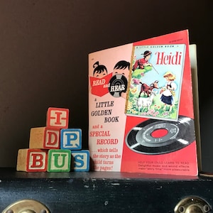 May include: A vintage children's book titled "Heidi" with a matching record. The book cover features a colorful illustration of children and goats. Wooden alphabet blocks spell out "IDP BUS" in red, blue, green, and white.