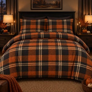 May include: A bedding set featuring a plaid pattern in shades of burnt orange, black, and cream. The set includes a duvet cover and two matching pillow shams, all displaying a consistent grid design with intersecting horizontal and vertical lines.