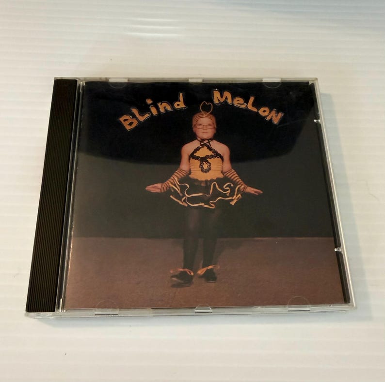 May include: A CD case featuring the album cover for Blind Melon. The cover art shows a young girl in a bee costume against a dark background. The band's name is written in orange letters at the top.