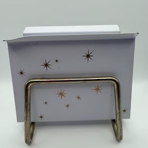 May include: A white metal recipe box with a gold starburst pattern. The box has a silver metal stand. The box is designed to hold recipe cards. The box is a vintage style.