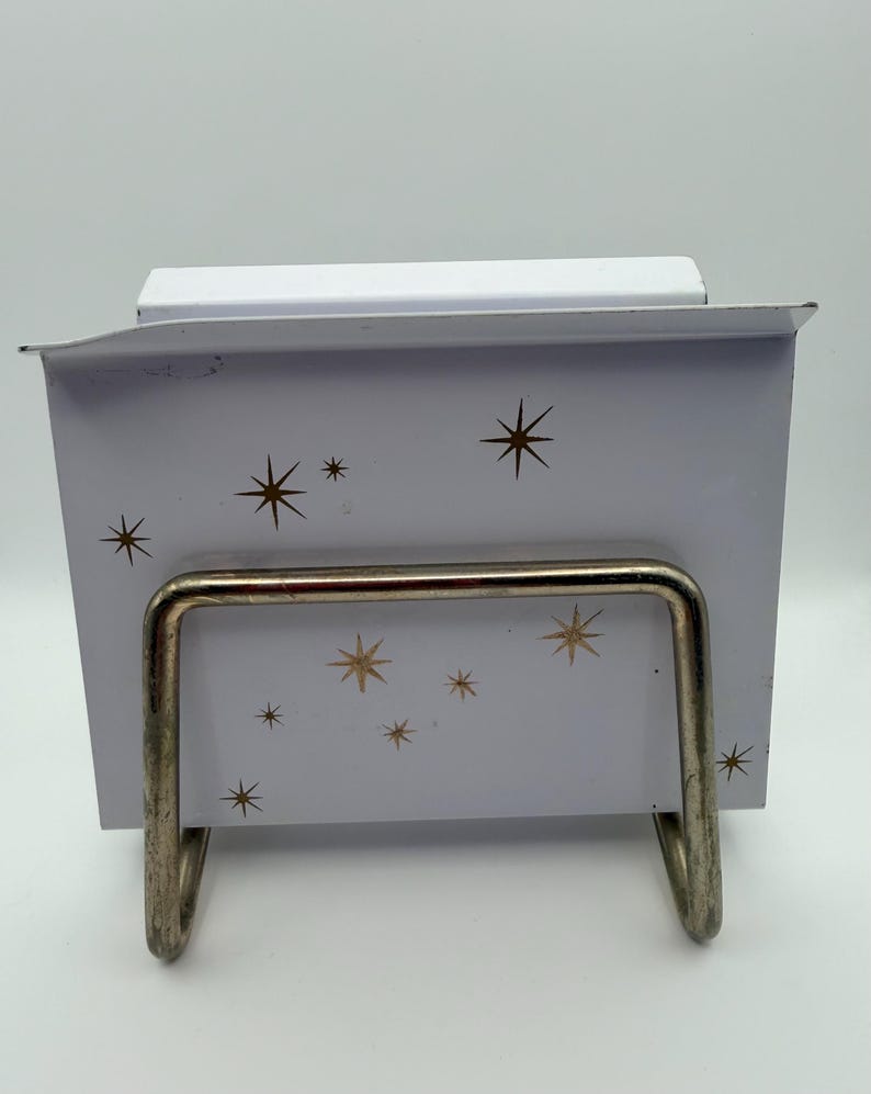 May include: A white metal recipe box with a gold starburst pattern. The box has a silver metal stand. The box is designed to hold recipe cards. The box is a vintage style.