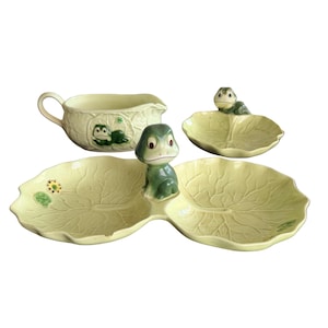 May include: A ceramic serving set featuring a light yellow gravy boat with a green frog, a small leaf-shaped dish with a green frog, and a double-sectioned leaf-shaped tray with a central green frog figure. Each piece has embossed leaf vein details.