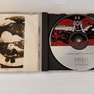 May include: Opened CD case with a disc featuring a red and black illustration of a woman and a creature. The CD case also has a black and white illustration of a person in a black coat. The text "amazing pumpkin * nanase dream" is visible on the CD.
