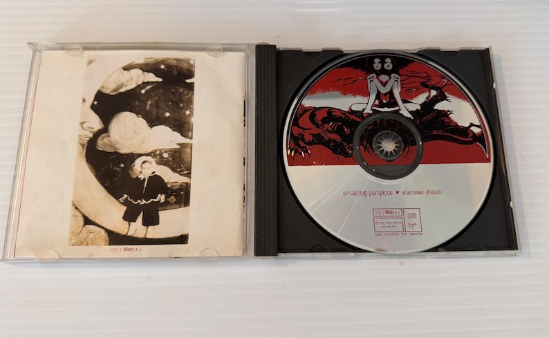 May include: Opened CD case with a disc featuring a red and black illustration of a woman and a creature. The CD case also has a black and white illustration of a person in a black coat. The text "amazing pumpkin * nanase dream" is visible on the CD.