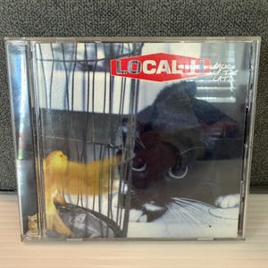 May include: A CD case featuring the album "Back Up the Cats" by Local H. The cover art shows a yellow bird in a cage and a black and white cat. The band's name is in a red and white logo.