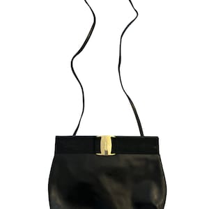 May include: Black leather shoulder bag with a gold-tone clasp. The bag features a black strap and a wide black band across the top. The bag is a classic design, suitable for everyday use.