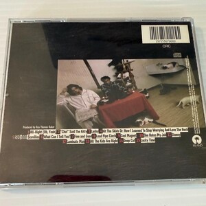 May include: A compact disc case with a black background and a photograph of a room with people and a table. The back of the CD case has a tracklist with song titles and the text "ISLAND".