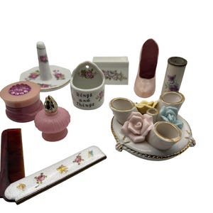 May include: A collection of vanity accessories including a ring holder, a small ceramic dish labeled Rings and Things, a pink shoe-shaped trinket holder, a floral comb, a perfume bottle, and a multi-cup ceramic organizer with sculpted roses.
