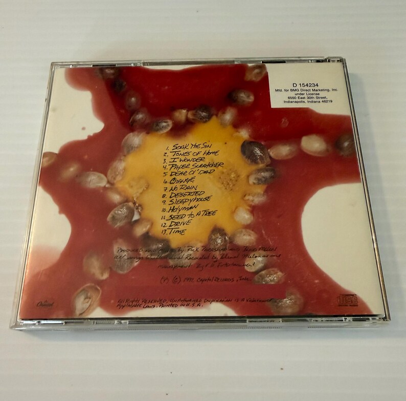 May include: A CD case featuring a colorful design with a red and yellow background and a pattern of seeds. The tracklist includes titles like "Soak the Sun" and "Seed to a Tree". The CD case is in a clear plastic case.